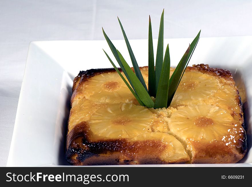 A dish of upside down pineapple pudding. Ingredients include pineapple, milk, syrup, butter, flour and eggs.