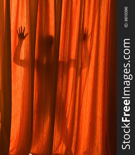 Silhouette of a girl outlined on a red curtain.