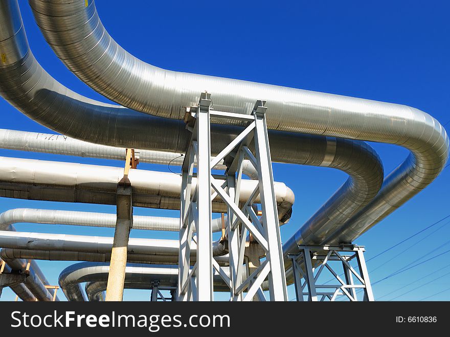 Industrial pipelines on pipe-bridge against blue sky.