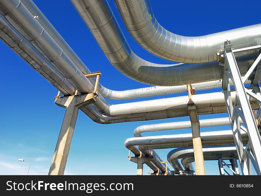 Industrial pipelines on pipe-bridge against blue sky.