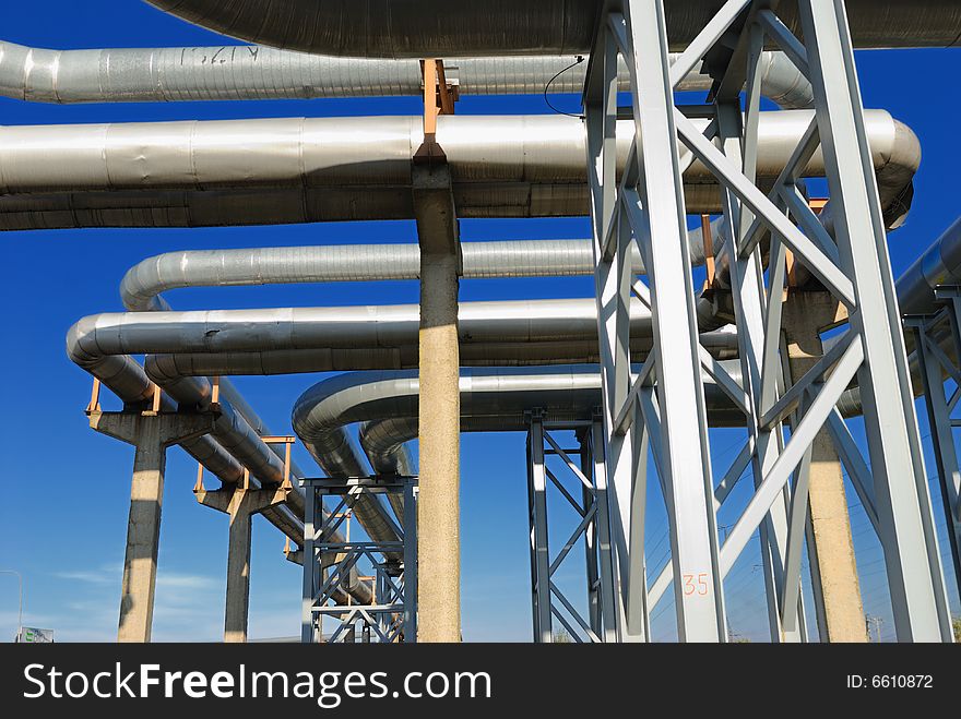 Industrial pipelines on pipe-bridge against blue sky.