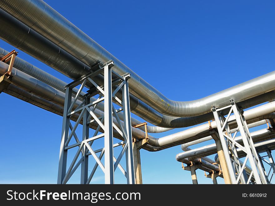 Industrial pipelines on pipe-bridge against blue sky.