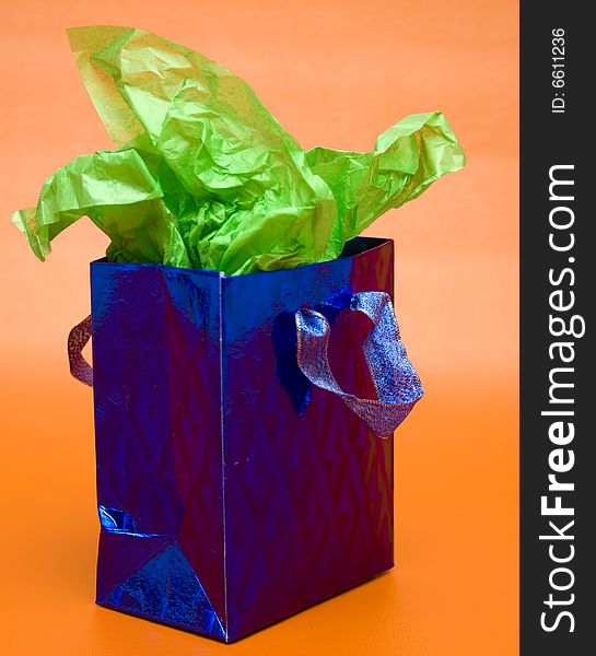 Shiny blue gift bag with green tissue paper against an orange background.