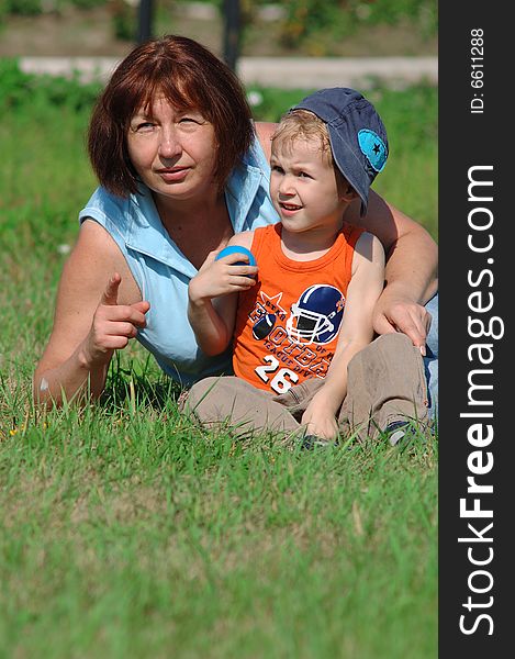 Grandmother and grandson are sitting on the green grass