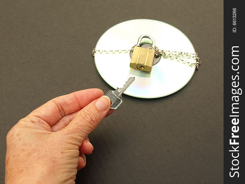 Photograph of hand holding a key and a CD with chain and padlock. Dark background. Photograph of hand holding a key and a CD with chain and padlock. Dark background.