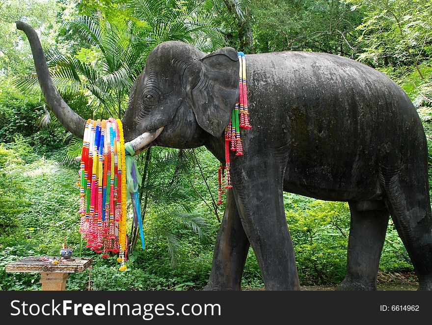 A Buddhist offering shrine in Thailand, with garlands of flowers draped over the trunk of an elephant sculpture. A Buddhist offering shrine in Thailand, with garlands of flowers draped over the trunk of an elephant sculpture.
