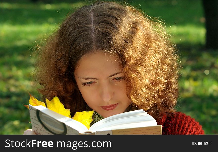 Young curly girl reads a book in a city park. The book contains a bright yellow autumn leaf. The girl is dressed in a vintage red coat. Sunlight on the grass.
. Young curly girl reads a book in a city park. The book contains a bright yellow autumn leaf. The girl is dressed in a vintage red coat. Sunlight on the grass.