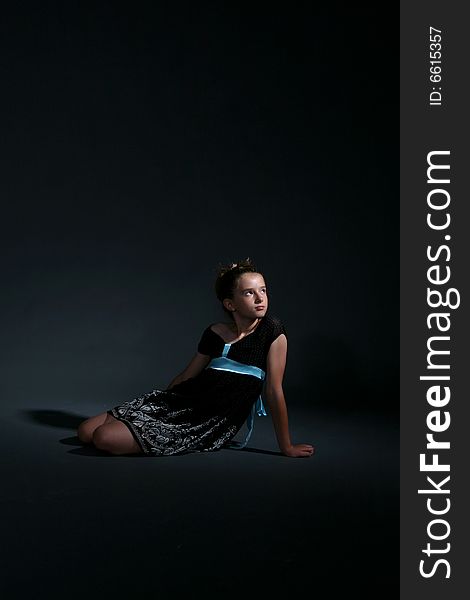 Pretty girl in black dress sitting on dark background. Pretty girl in black dress sitting on dark background