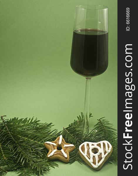 A glass of red wine and two cookies on a fir branch isolated on green paper. A glass of red wine and two cookies on a fir branch isolated on green paper