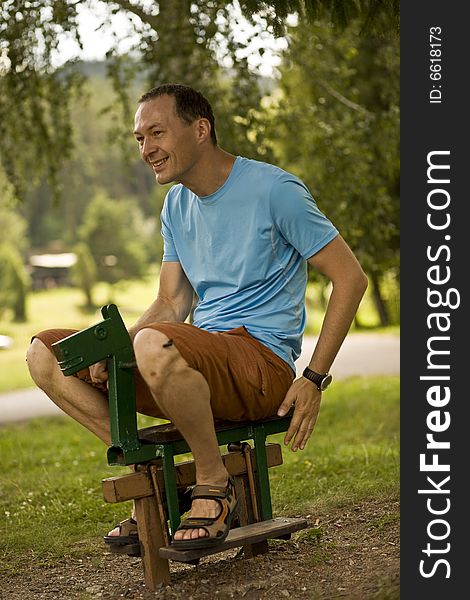 A man enjoying riding a small wooden horse at playground. A man enjoying riding a small wooden horse at playground.