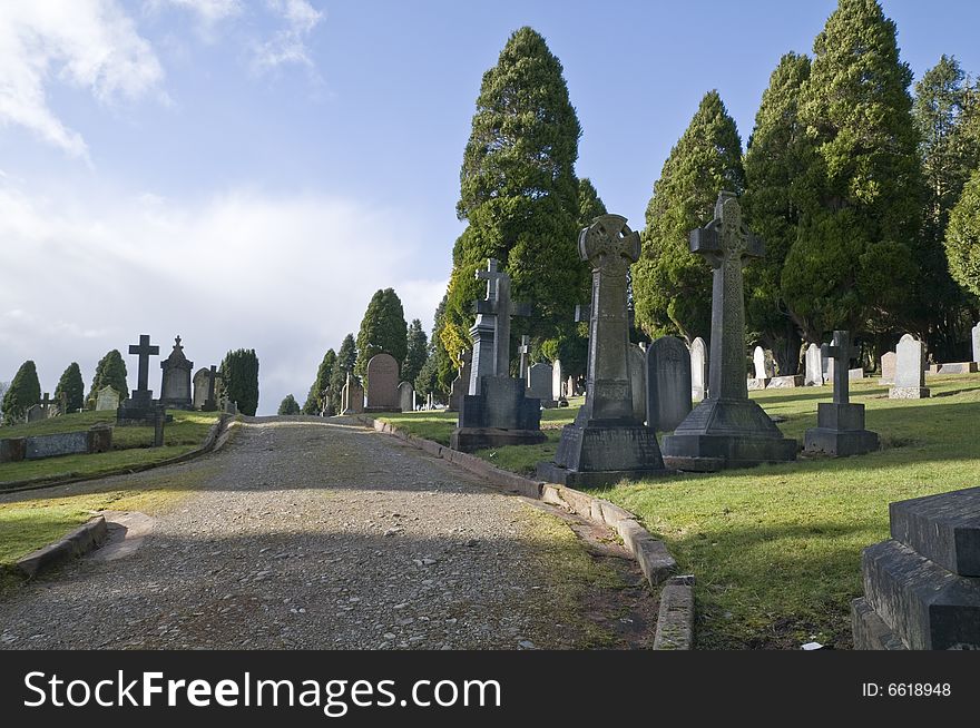 Footpath through a graveyard, surrounded by gravestones and trees. Footpath through a graveyard, surrounded by gravestones and trees.
