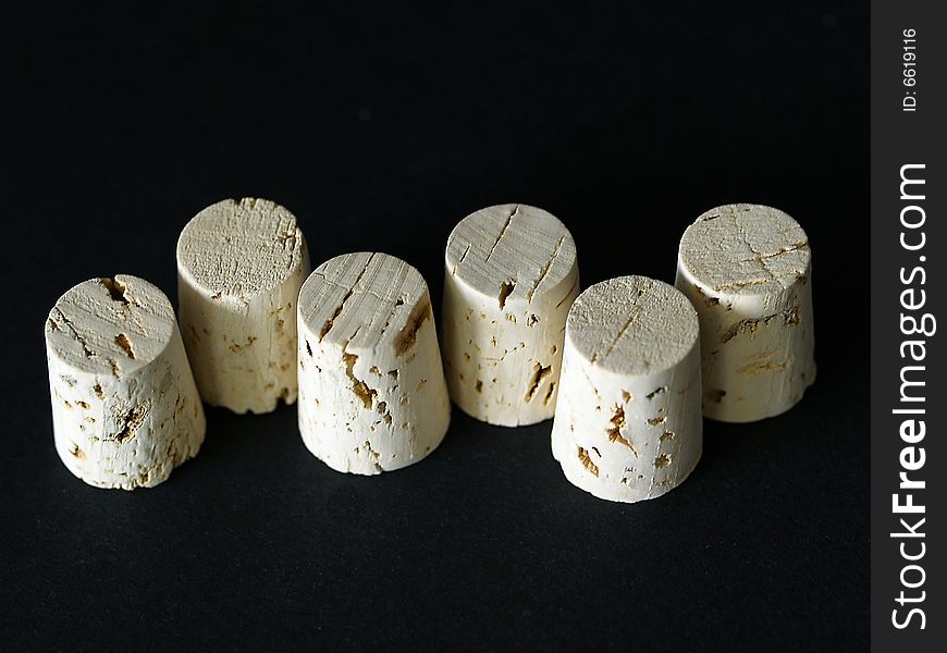 Six small vine bottle corks isolated on a black background