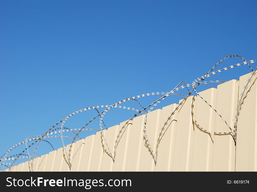 Fragment of fence with barbed wire on blue sky background. Fragment of fence with barbed wire on blue sky background