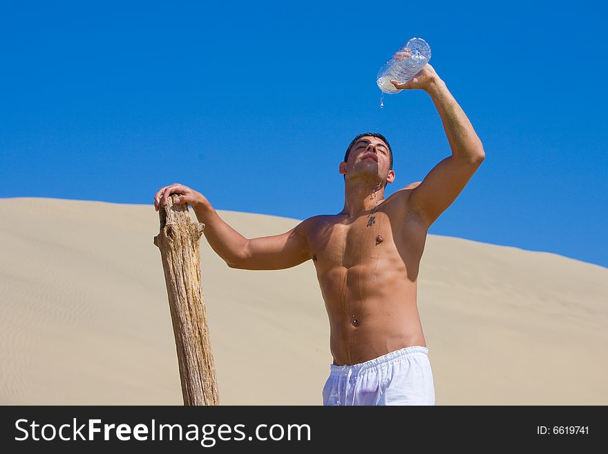 Young atlethic man refreshing with water on desert dune. Young atlethic man refreshing with water on desert dune