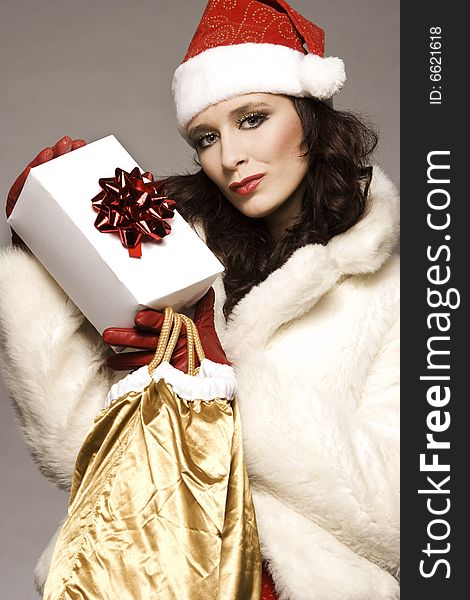 Beautiful brunette girl wearing Santa costume holding Christmas present on grey background. Beautiful brunette girl wearing Santa costume holding Christmas present on grey background