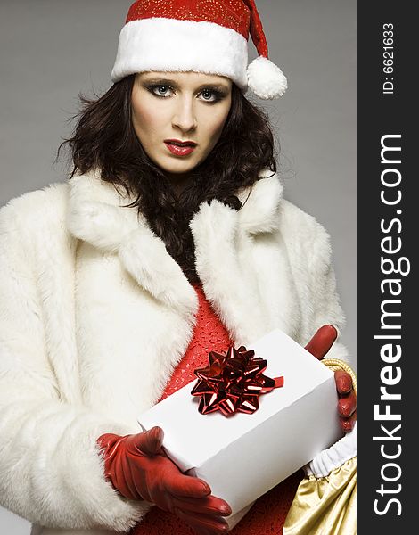 Beautiful brunette girl wearing Santa costume holding Christmas present on grey background. Beautiful brunette girl wearing Santa costume holding Christmas present on grey background