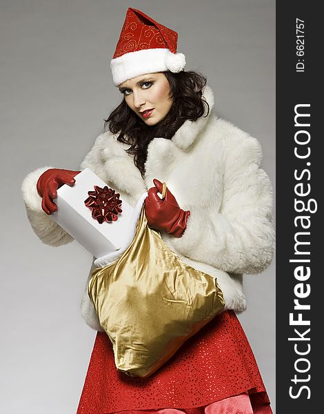 Beautiful brunette girl wearing Santa costume holding Christmas present on grey background. Beautiful brunette girl wearing Santa costume holding Christmas present on grey background