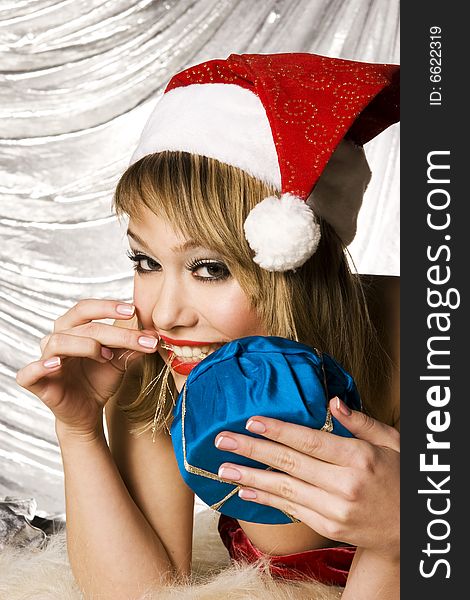Beautiful blonde girl wearing Santa costume holding Christmas present on silver background. Beautiful blonde girl wearing Santa costume holding Christmas present on silver background