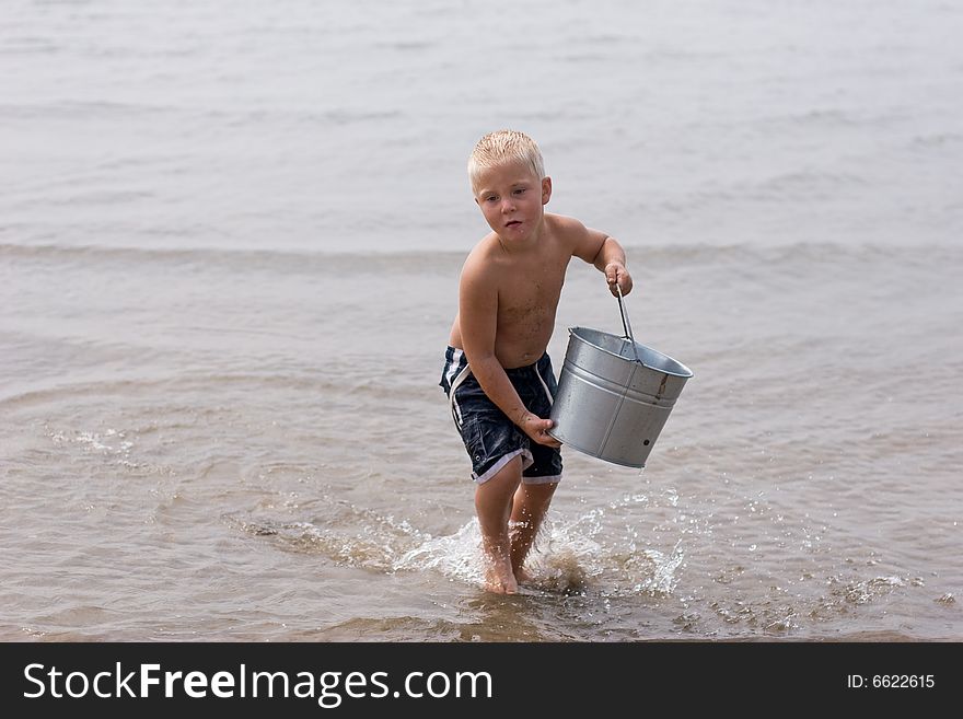 Boy carrying water in his bucket at the beach. Boy carrying water in his bucket at the beach