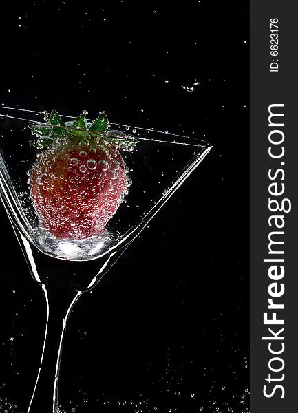 View of martini glass with strawberry on black background. View of martini glass with strawberry on black background