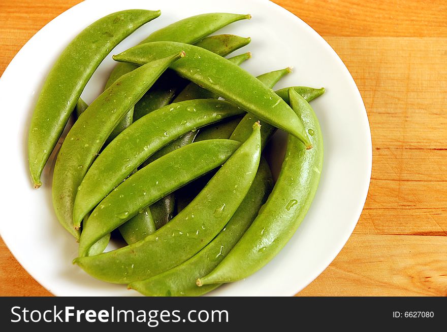 Green snap peas on wooden cutting board