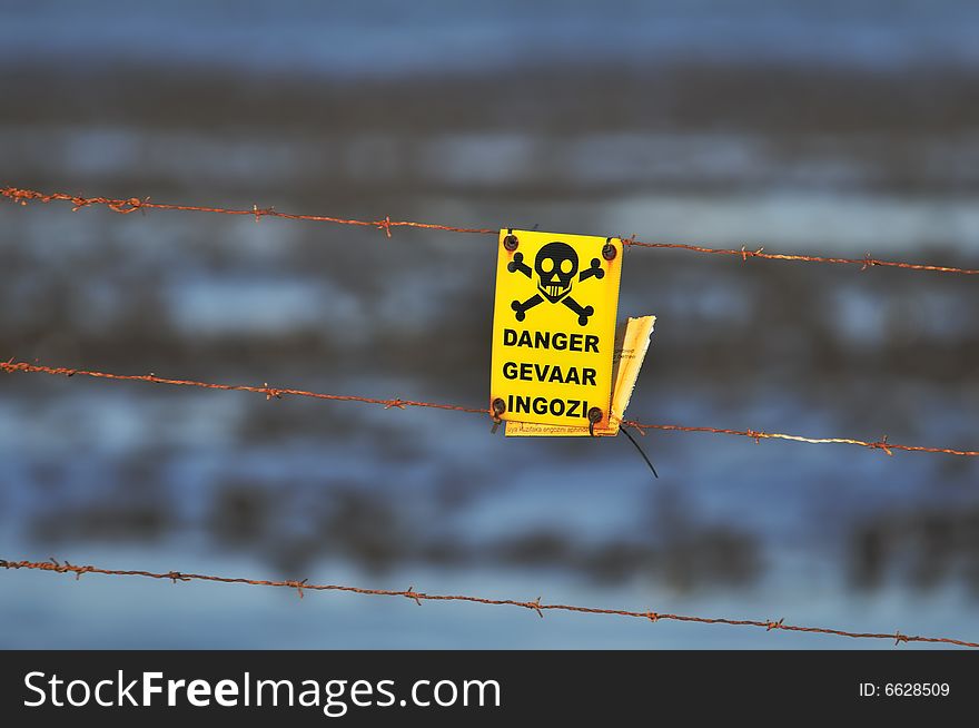 A danger sign attached to a rusty barb wire ensures people can't enter the wild sea behind it