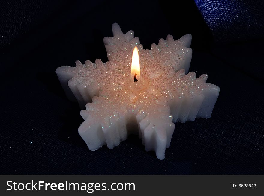 Snowflake-shaped candle on the dark background. Narrow depth of field. Snowflake-shaped candle on the dark background. Narrow depth of field.