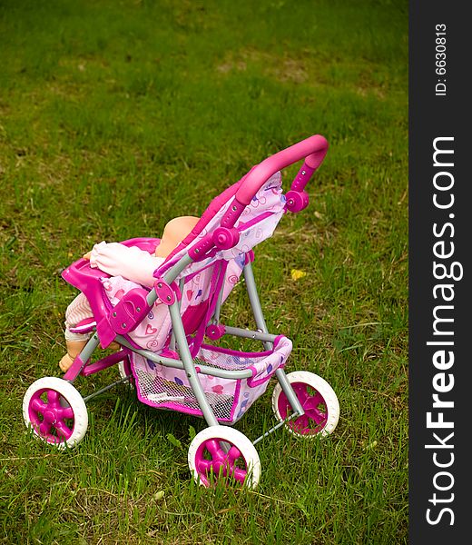 Pink toy pram on green grass
