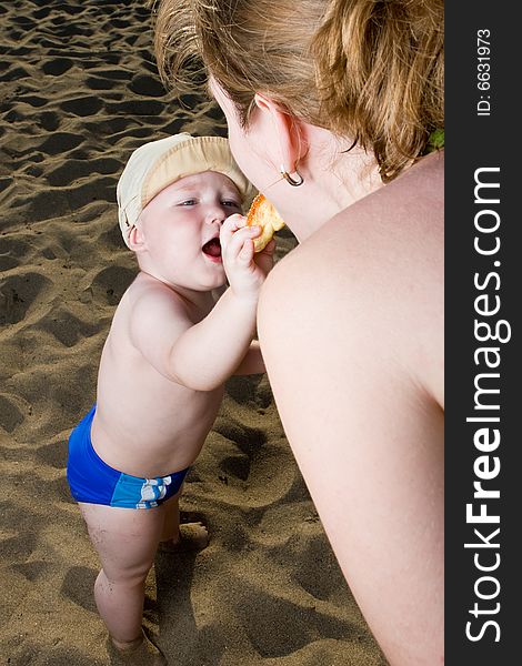 Young child on a beach treats mum with a cake. Young child on a beach treats mum with a cake