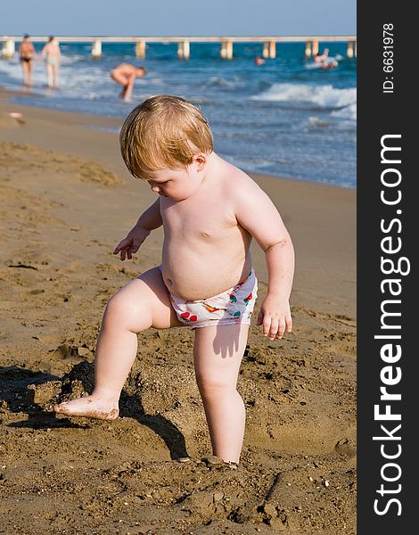 Small child stands on one leg on a beach