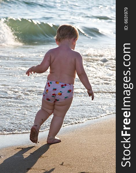 Child runs on a beach on a background of waves