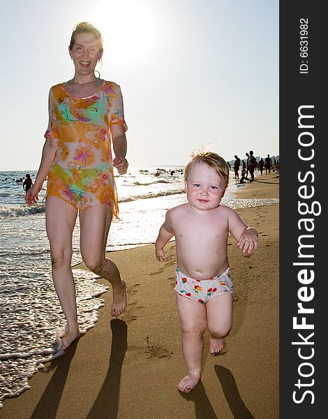 Woman and the child run on a beach on a background of the sea