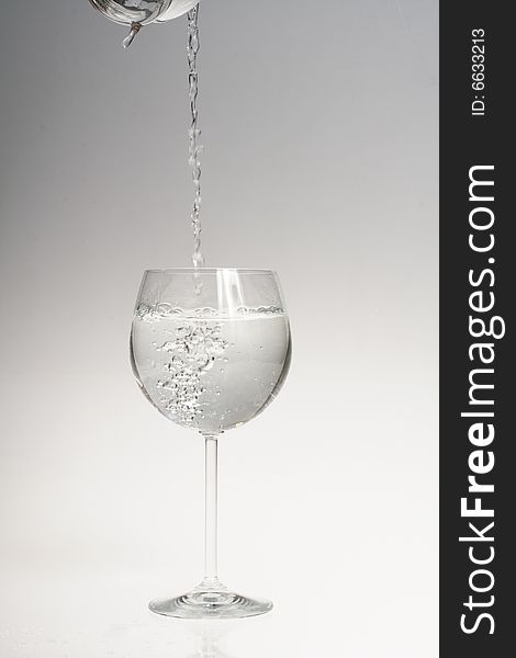 Water poured into wine glass on gradient background from grey to white. Water poured into wine glass on gradient background from grey to white