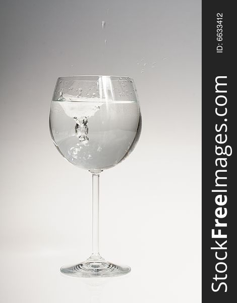 Water splash in wine glass on gradient background from grey to white. Water splash in wine glass on gradient background from grey to white