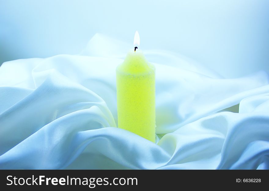 Burning candle on white silk