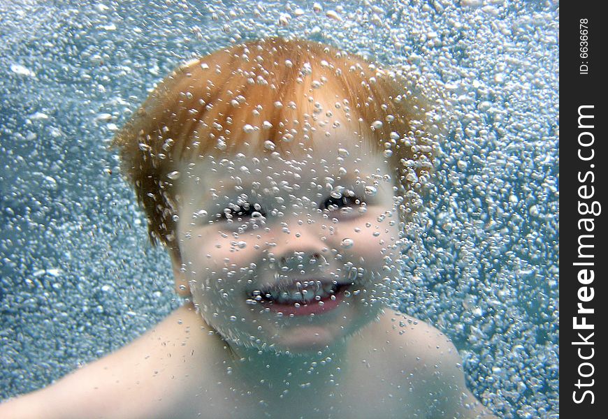 Portrait of a 2 yr old boy jumping into the pool, smiling at the camera through a curtain of bubbles. Portrait of a 2 yr old boy jumping into the pool, smiling at the camera through a curtain of bubbles