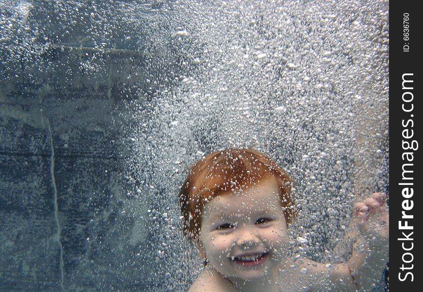 Portrait of a 2 yr old boy jumping into the pool, smiling at the camera through a curtain of bubbles. Portrait of a 2 yr old boy jumping into the pool, smiling at the camera through a curtain of bubbles