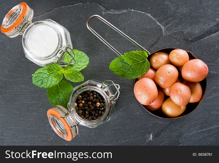 New potatoes in a small pan with salt, pepper and mint on a slate background. New potatoes in a small pan with salt, pepper and mint on a slate background