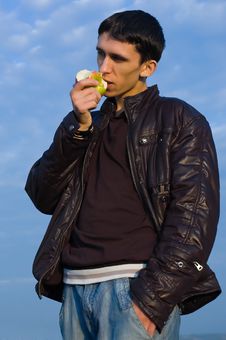 Young Man Eats An Apple Against The Blue Sky Royalty Free Stock Photography