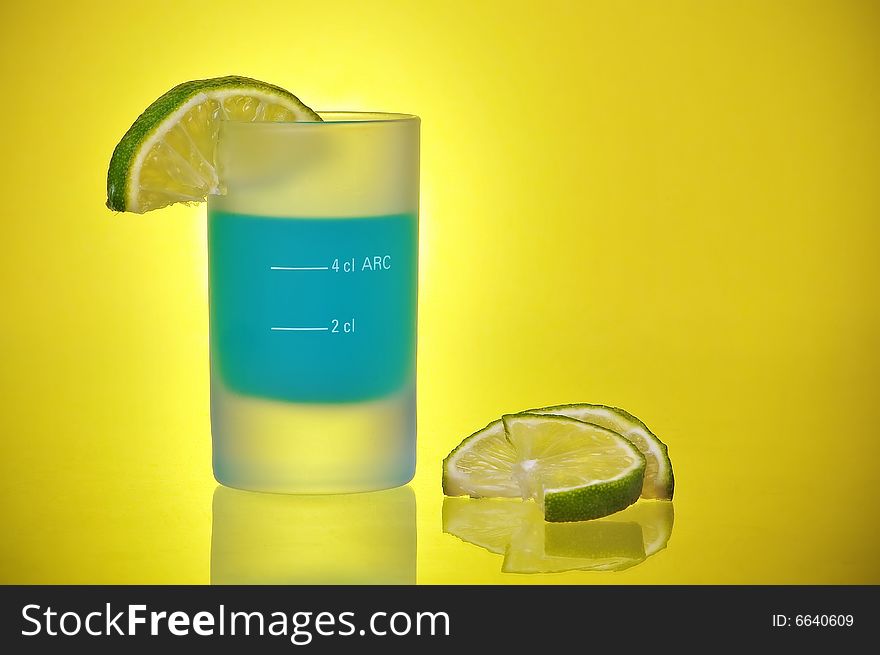 Shot Glass With Blue Tequila Liquor Shooter and Lime Slices on a yellow gradient background. Shot Glass With Blue Tequila Liquor Shooter and Lime Slices on a yellow gradient background