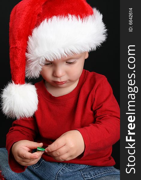 Blonde toddler against a black background with a christmas hat