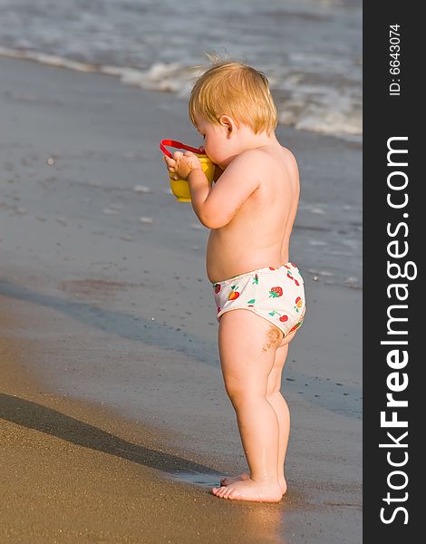 Child stands on a beach and drinks from a bucket