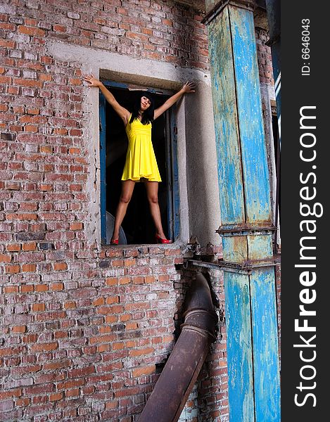 The young girl standing on a window sill of an open window of the old factory located in a building