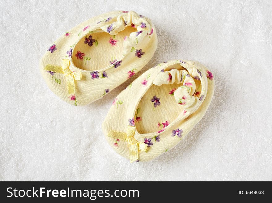 Small yellow children's bootees stand together on a white fabric. Small yellow children's bootees stand together on a white fabric