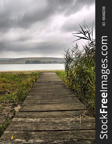 Wooden jetty on over the  beach with grey sky and clouds near the lake in the middle of autumn