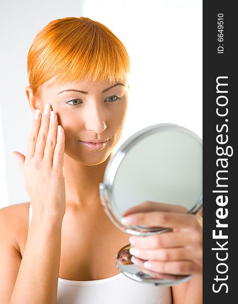 Young woman looking in mirror and touching her face. Front view. Young woman looking in mirror and touching her face. Front view.