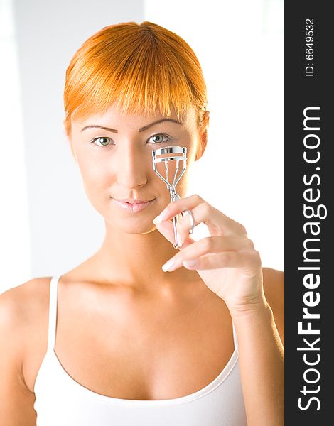 Young woman curling her eyelashes. She's looking at camera. Front view. Young woman curling her eyelashes. She's looking at camera. Front view.