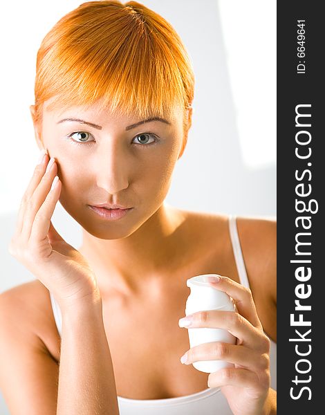 Beauty woman applying face cream. She's looking at camera. Front view.