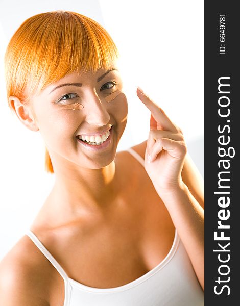 Young red-haired woman put cream on face. She's smiling and looking at camera. Closeup on face. Young red-haired woman put cream on face. She's smiling and looking at camera. Closeup on face.