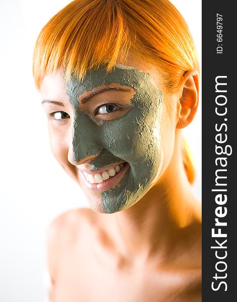 Young red-haired woman with green mask on half face. She's smiling and looking at camera. Closeup on face. Young red-haired woman with green mask on half face. She's smiling and looking at camera. Closeup on face.